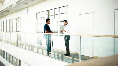 Zwei Ärzte im Gespräch im Krankenhausflur, helles, offenes Gebäude