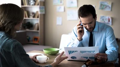 Paar sitzt am Esstisch, der Mann arbeitet und telefoniert, die Frau empört