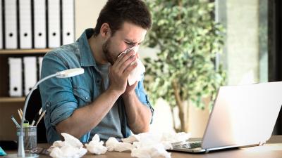 Erkälteter Mann arbeitet am Laptop