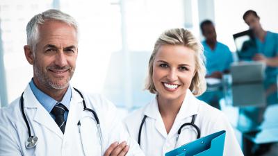 Ältere Ärzt und junge Ärztinn stehen lächelnd nebeneinander