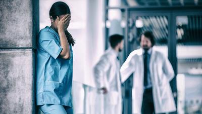 Traurige junge Ärztin, Kollegen im Hintergrund