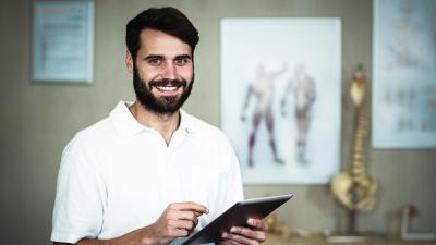 junger lächelnder Arzt mit Tablet in der Hand in einer Arztpraxis