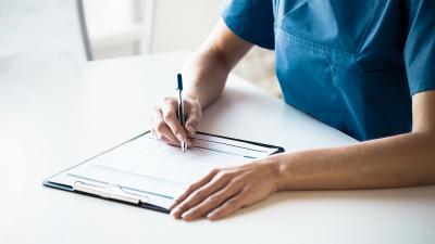 Person schreibt auf Zettel im Klemmbrett