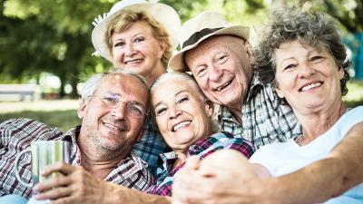 Gruppe älterer Menschen in Freizeitkleidung, entspannt im Freien sitzend, umgeben von grüner Natur und sommerlicher Atmosphäre.