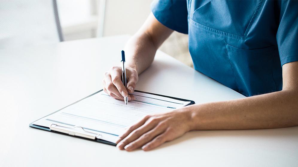 Person schreibt auf Zettel im Klemmbrett